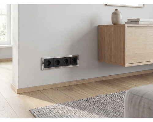 Schwarze 4-fach Steckdose mit verchromtem Rahmen, horizontal an einer hellen Wand in einem modernen Wohnzimmer montiert.