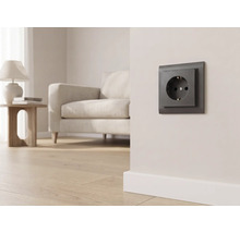 Dunkle Steckdose an einer hellen Wand in einem modern eingerichteten Wohnzimmer mit Sofa und Parkettboden.