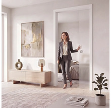 Moderne, helle Inneneinrichtung mit einer Frau, die durch eine Glasschiebetür geht. Wohnzimmer mit Holzkommode und abstrakter Kunst.