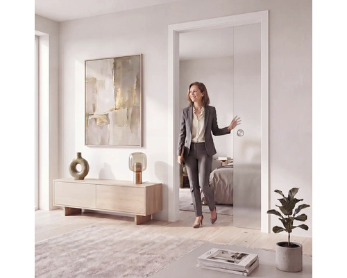 Moderne, helle Inneneinrichtung mit einer Frau, die durch eine Glasschiebetür geht. Wohnzimmer mit Holzkommode und abstrakter Kunst.