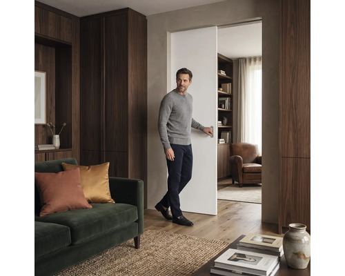 Ein Mann bedient eine Schiebetür in einem modern eingerichteten Wohnzimmer mit Holzschränken und einem Sofa.