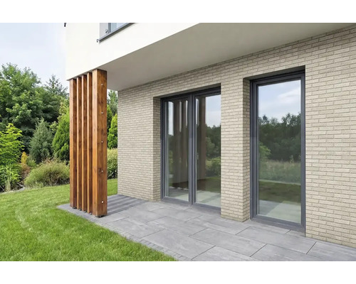 Fassade mit hellen Verblendsteinen in Klinkeroptik, bodentiefen Fenstern und einer Terrasse mit grauen Steinplatten.