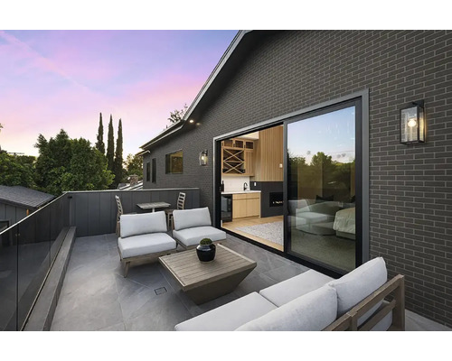 Moderne Dachterrasse mit grauer Klinkerfassade, Glasschiebetür, Lounge-Möbeln und Glasgeländer.