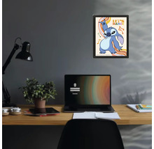 Gerahmtes Poster mit Disney-Figur Stitch und Schriftzug Let's Dance über einem Schreibtisch mit Laptop und Lampe in einem modernen Arbeitszimmer.