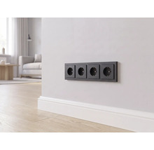 Eine 4-fach Steckdose in Schwarz an einer hellen Wand über einer weißen Fußleiste in einem modern eingerichteten Wohnzimmer.