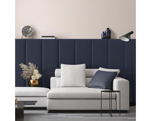 Modernes Wohnzimmer mit dunkelblauen gepolsterten Wandpaneelen, einem hellgrauen Sofa mit Kissen, einem schwarzen Beistelltisch und einer Stehlampe.