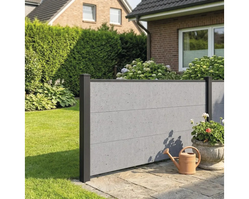 Moderner Sichtschutzzaun in Beton-Optik mit dunklen Pfosten in einem Garten auf einer Steinterrasse neben einer Gießkanne.