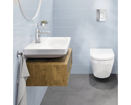 Modernes, helles Badezimmer mit Keramik-Waschbecken auf Holz-Unterschrank, verchromter Armatur und Wand-WC vor gefliesten Wänden.
