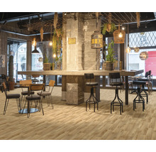 Industrie-Restaurant mit hellem Boden in Holzoptik, Betonsäulen, Barhockern aus Metall und hängenden Leuchten.