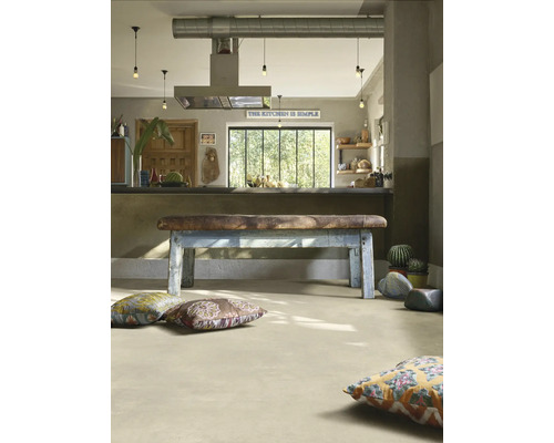 Industrielle Wohnküche mit hellem Boden in Betonoptik, Vintage-Sitzbank aus Leder und Holz sowie bunten Bodenkissen.