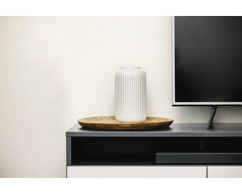 Geriffelte Vase auf einem flachen Holzteller neben einem Fernseher auf einem modernen Sideboard.
