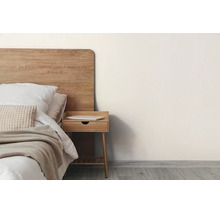 Minimalistisches Schlafzimmer mit hölzernem Kopfteil, Bett mit weißer Bettwäsche und beigefarbenem Überwurf sowie einem hölzernen Nachttisch.
