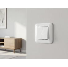 Weißer Doppel-Lichtschalter an einer hellen Wand in einem hellen, modern und organisiert eingerichteten Raum.