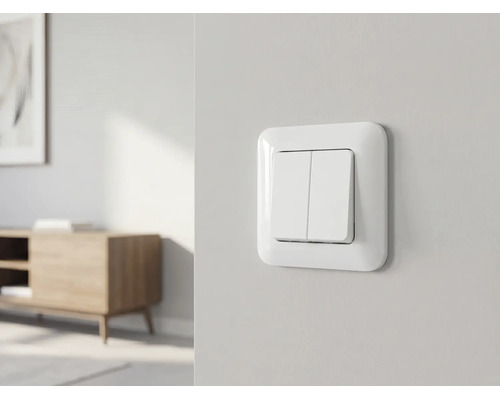 Weißer Doppel-Lichtschalter an einer hellen Wand in einem hellen, modern und organisiert eingerichteten Raum.