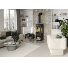 Modernes Wohnzimmer mit schwarzem Kaminofen vor einer Natursteinwand, hellem Sofa, grauem Couchtisch und weißem Sessel.