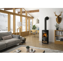 Moderner schwarzer Kaminofen mit brennendem Feuer in einem hellen Wohnzimmer mit Sofa, Holztisch und großen Panoramafenstern mit Schneeblick.