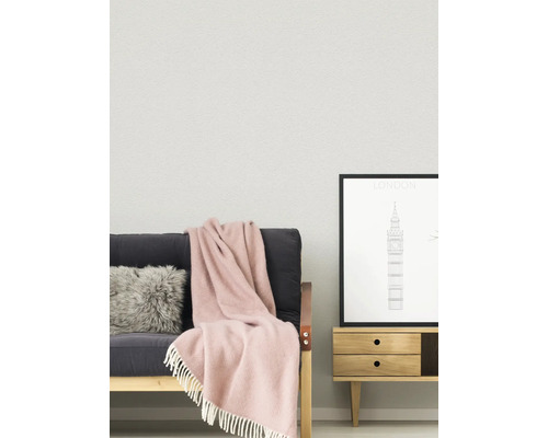Helles, organisiertes Wohnzimmer mit strukturierter Wand, einem Sofa mit Fellkissen und Fransendecke sowie einem Beistelltisch aus Holz mit Poster.