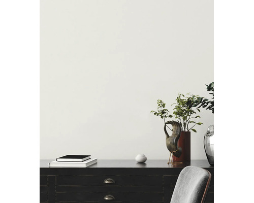Helle minimalistische Szene mit einer hell gestrichenen Wand, einem dunklen Holzschreibtisch mit Dekoration, Büchern und einer Pflanze in einer Vase.