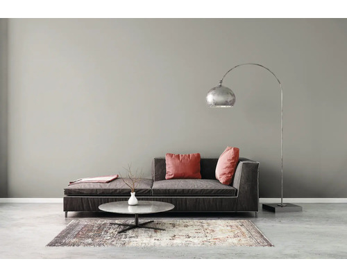 Modernes Wohnzimmer mit grauer Wand, dunklem Sofa, Bogenlampe und Marmor-Couchtisch auf gemustertem Teppich und Betonboden.