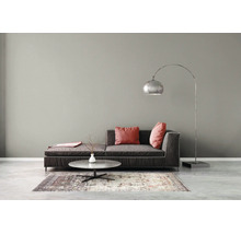 Modernes Wohnzimmer mit grauer Wand, dunkelgrauem Sofa, roten Kissen, silberner Bogenlampe und rundem Couchtisch auf einem gemusterten Teppich.