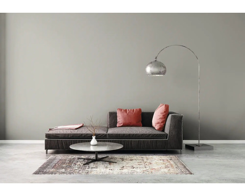 Modernes Wohnzimmer mit grauer Wandfarbe, dunklem Sofa mit roten Kissen, rundem Couchtisch, gemustertem Teppich und einer Bogenstehlampe.