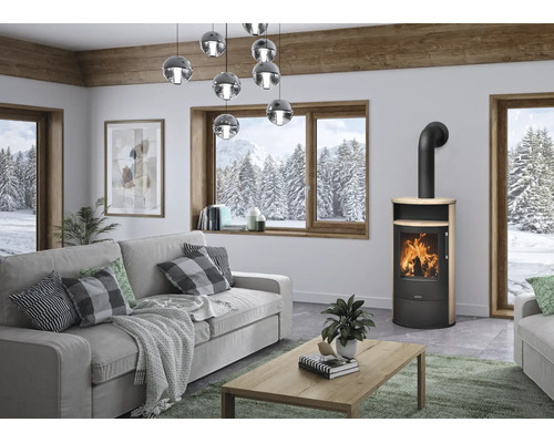 Moderner Kaminofen aus schwarzem Metall und Holz in einem hellen Wohnzimmer mit grauem Sofa und großen Fenstern mit Bergblick.