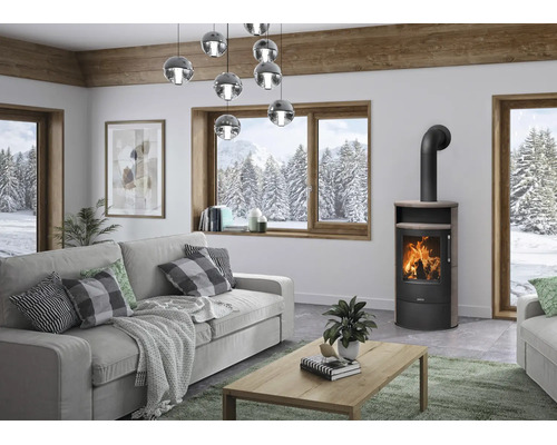 Moderner Kaminofen in hellem Wohnzimmer mit Blick auf verschneite Winterlandschaft durch ein großes Holzfenster.