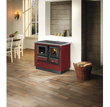 Roter Holzherd mit Backofen und Sichtscheibe in einer modernen, hellen Küche mit Holzboden und einem Korb voller Kaminholz.