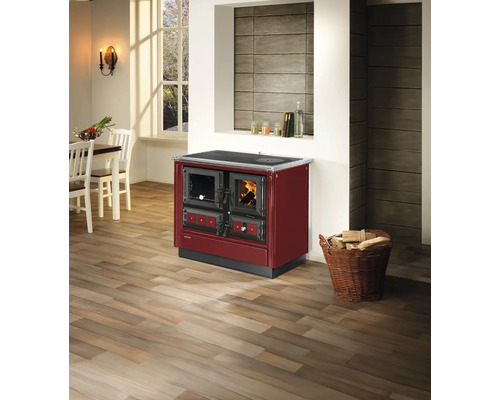Roter Holzherd mit Backofen und Sichtscheibe in einer modernen, hellen Küche mit Holzboden und einem Korb voller Kaminholz.