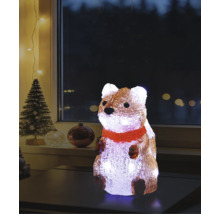 Beleuchtete Acrylfigur Eichhörnchen mit rotem Schal auf einem Tisch, Weihnachtsdekoration für den Innenbereich mit Tannenbaum im Hintergrund.