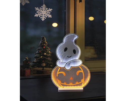 LED-Halloween-Dekoration Geist auf Kürbis mit Infinity-Effekt vor einem Fenster neben einem geschmückten Tannenbaum.