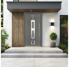 Moderne graue Hauseingangstür mit Glaseinsätzen und langem Stangengriff an einem hellen Hauseingang mit Betontreppen und Pflanzen.