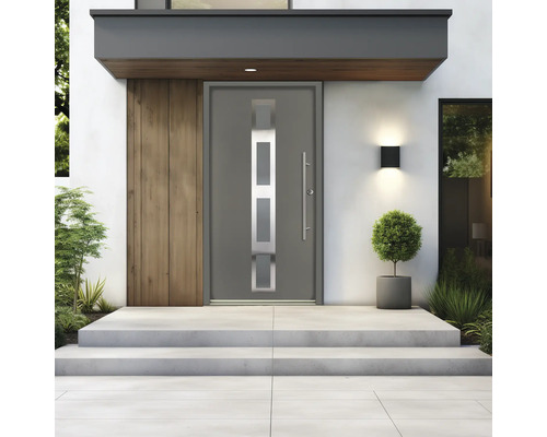 Moderne graue Hauseingangstür mit Glaseinsätzen und langem Stangengriff an einem hellen Hauseingang mit Betontreppen und Pflanzen.