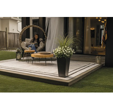 Moderne Terrasse mit Outdoorteppich, runden Holztischen, einem Hängesessel und einem hohen Pflanzgefäß mit Blumen und Gräsern.