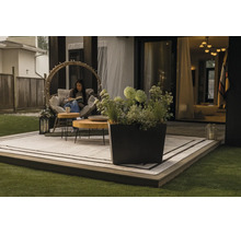Eingerichtete Terrasse mit quadratischem Pflanzkübel, kreisförmigem Gartensessel, Holztischen und Outdoor-Teppich auf einem Holzdeck.