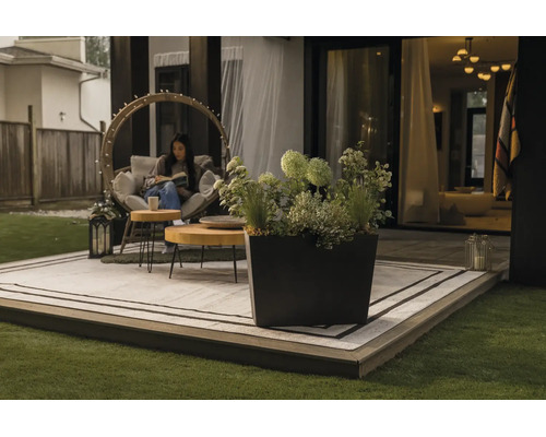 Eingerichtete Terrasse mit quadratischem Pflanzkübel, kreisförmigem Gartensessel, Holztischen und Outdoor-Teppich auf einem Holzdeck.
