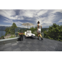 Moderne Dachterrasse mit dunklen WPC-Klickfliesen, Glasgeländer, Sonnenliege, Sonnenschirm und Pflanzgefäß mit Blick auf die Natur.