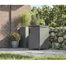 Moderne Mülltonnenbox aus Metall und passender Pflanzkübel auf einer gepflasterten Terrasse neben einer Ziegelwand und einer Natursteinmauer.
