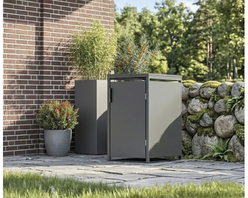 Moderne Mülltonnenbox aus Metall und passender Pflanzkübel auf einer gepflasterten Terrasse neben einer Ziegelwand und einer Natursteinmauer.