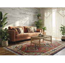 Helles Wohnzimmer im Boho-Stil mit Samtsofa, Rattan-Couchtisch und gemustertem Teppich. Grüne Zimmerpflanzen und Wandpaneele in Holzoptik.