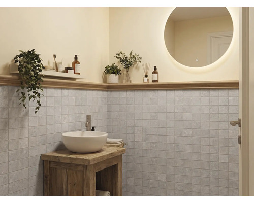 Modernes Badezimmer mit rundem beleuchtetem Spiegel, weißem Waschbecken auf rustikalem Holzschrank und grauen quadratischen Wandfliesen.