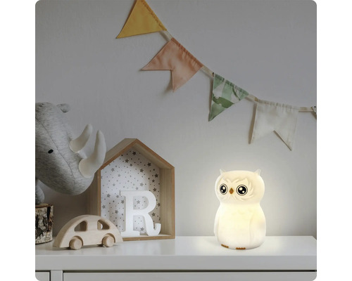 Eulenförmiges LED-Nachtlicht leuchtend in einem Kinderzimmer mit Holzspielzeug und Stoffwimpeln.