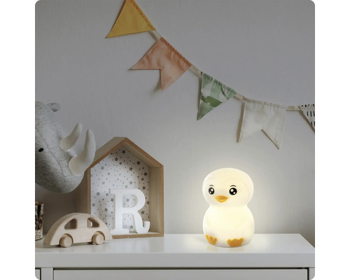 Leuchtendes LED-Nachtlicht in Pinguinform auf einem weißen Möbelstück im Kinderzimmer neben Holzspielzeug und einer Wimpelkette.