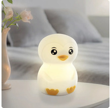 Pinguinförmiges Nachtlicht leuchtend auf einem Nachttisch neben einer Vase mit Rosen in einem hellen Schlafzimmer.