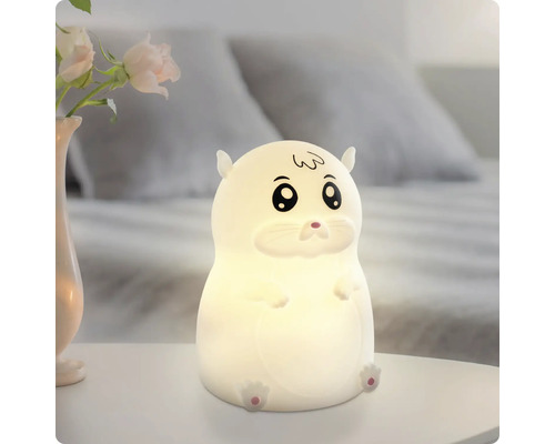 Leuchtendes LED-Nachtlicht in Hamsterform auf einem weißen Nachttisch in einem Schlafzimmer.