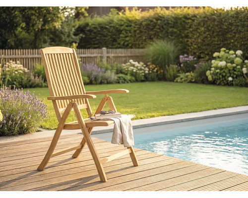 Klappbarer Gartenstuhl aus Holz mit Armlehnen auf einer Holzterrasse neben einem Pool im hellen, organisierten Garten.