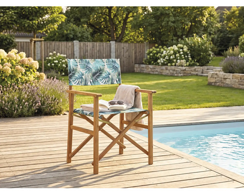 Klappstuhl aus Holz mit Palmenblattmuster auf einer Holzterrasse neben einem Pool im Garten.