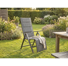 Gepolsterter Garten-Hochlehner mit verstellbarer Fußstütze in einem hellen Garten mit Rasen, Blumenbeeten und Holztisch.