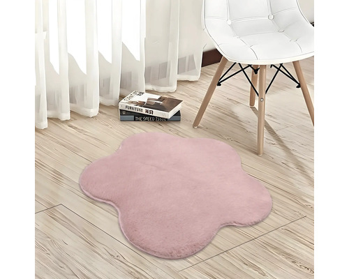 Blütenförmiger, weicher Teppich in Rosa auf hellem Holzboden neben einem Stuhl.
