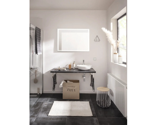 Modernes Badezimmer mit Aufsatzwaschbecken, beleuchtetem Spiegel, Waschtischplatte, Wäschesack, Heizkörper und Badaccessoires.